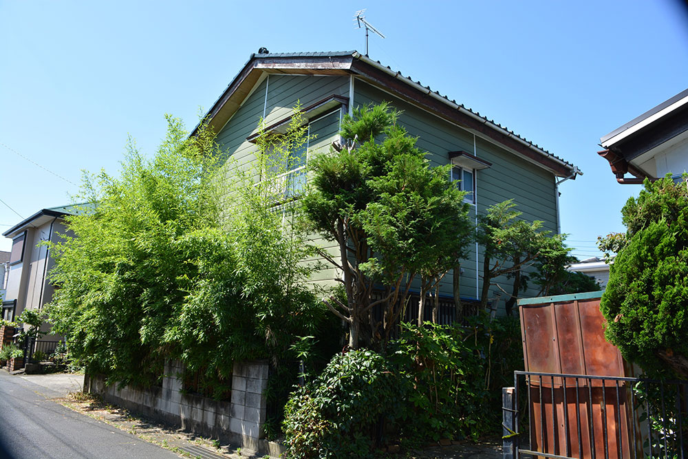 樹木が伸びたまま放置された相続空き家。残置物の片付けや相続登記もまとめて対応